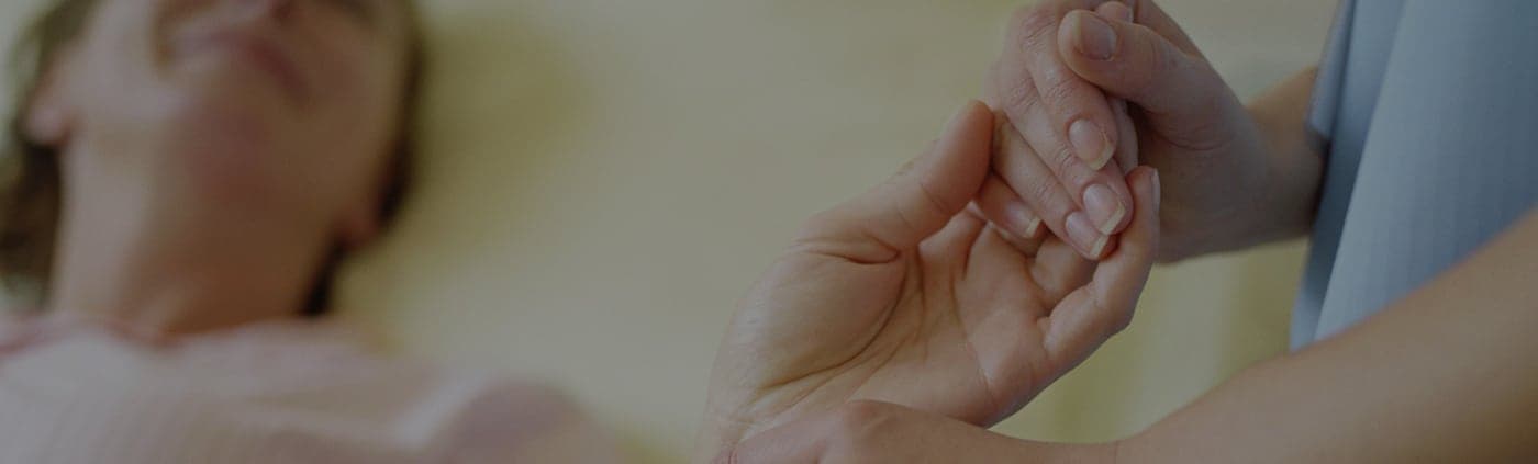 A nurse gently holding the hand of an older patient resting in bed
